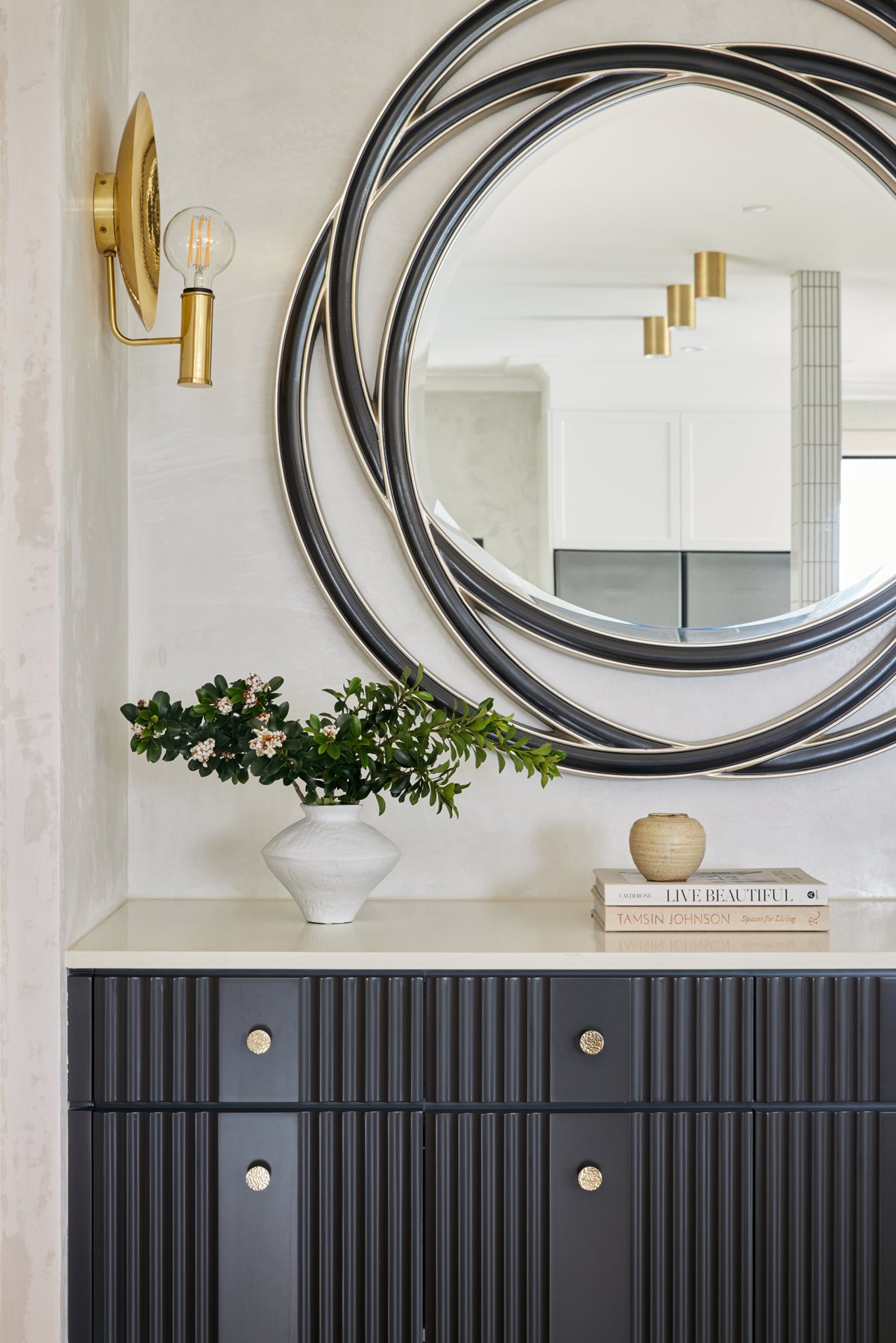 Brass wall sconce beside a round mirror