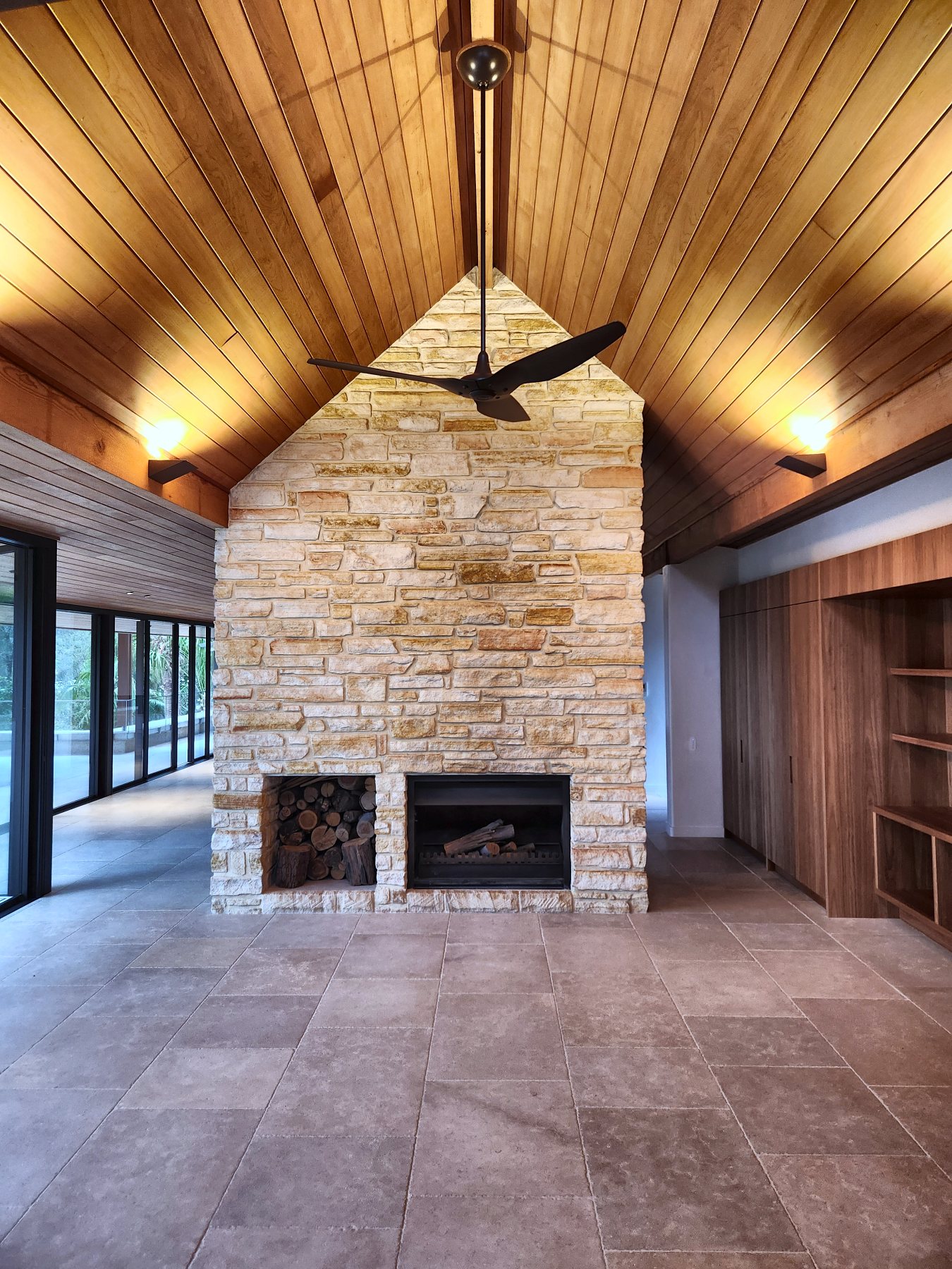 Sandstone fireplace under a vaulted timber ceiling with wall lights