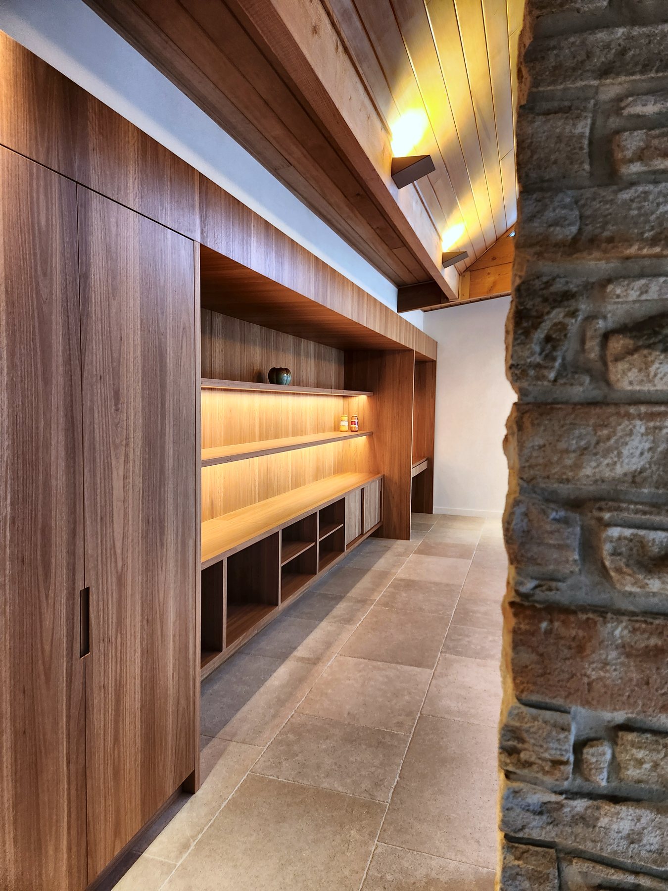 Joinery corridor with lit shelving beside a stone wall